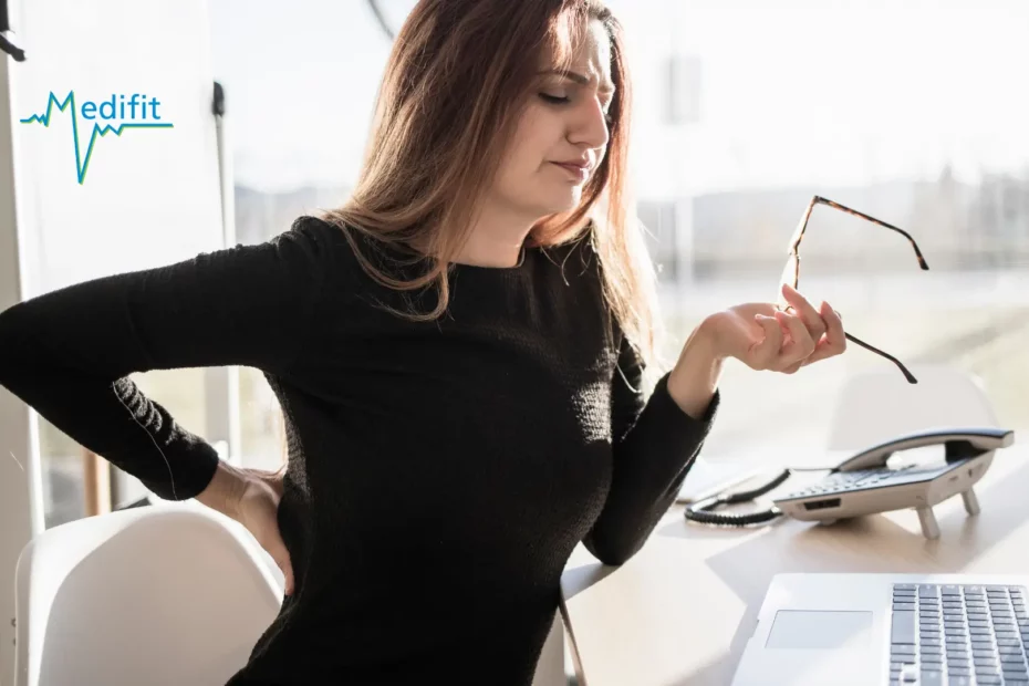 Femme assise à son bureau se tenant le bas du dos, douleur lombaire et prévention du mal de dos au bureau par Medifit Lausanne