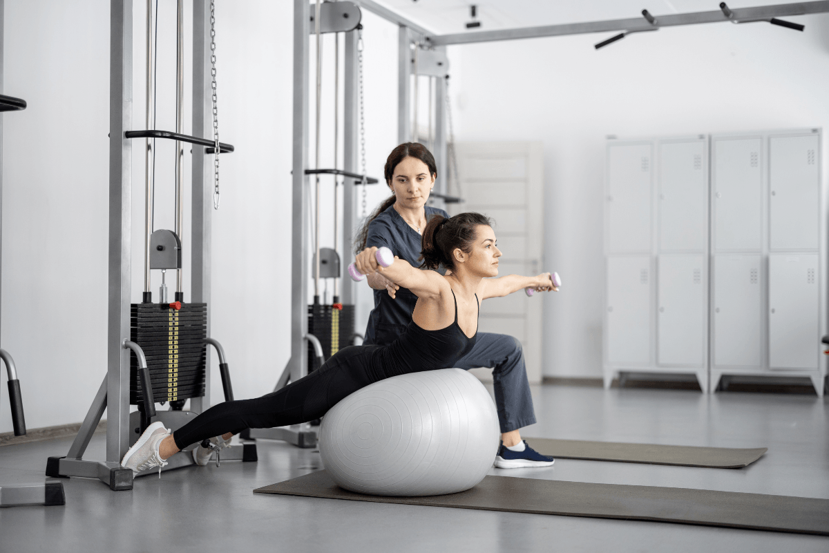 Rééducation fonctionnelle au centre de physio Lausanne : patiente en plein effort physique encadrée par sa physiothérapeute en salle de sport médicale.