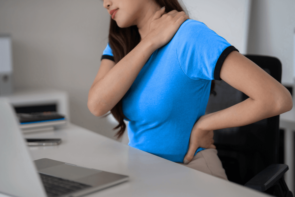 Jeune femme travaillant à son bureau devant un ordinateur et souffrant d'une douleur en bas du dos due à une position assise prolongée.