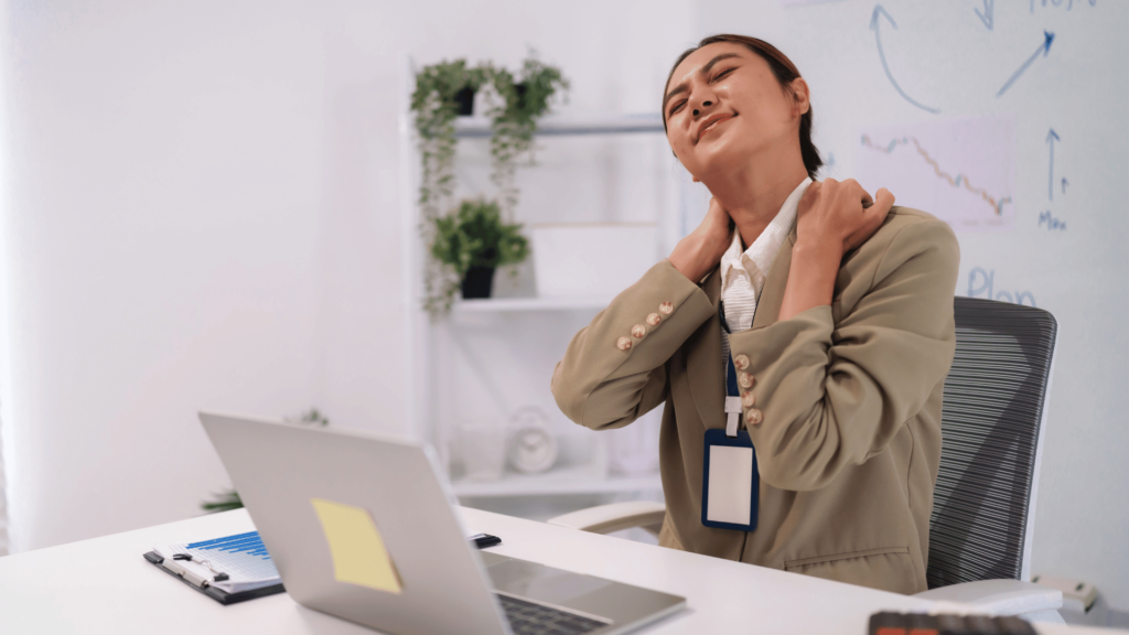 Femme au bureau souffrant d'une douleur à l'épaule et à la nuque due à une posture prolongée devant un ordinateur.